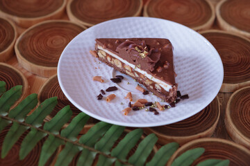 chocolate dessert in a cut with filling of caramel, nuts and nougats. The cake is covered with chocolate on a wooded background with a morning natural light
