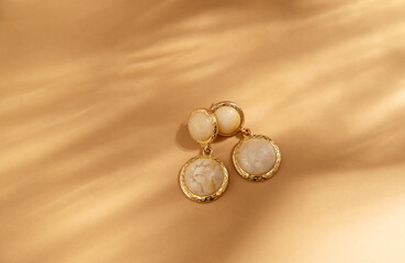 Fashionable gold handmade earrings on a beige background. wood cut. Flat lay, top view, minimalist fashion jewelry with shadows of sunlight.