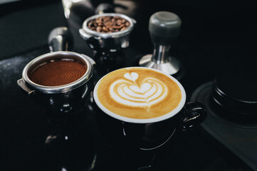 Selective focus Hot Coffee cup and beans and a portafilter with coffee beans, a portafilter with ground coffee on black table. Top view with copyspace for your text