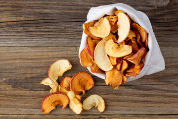 A pile of dried slices of apples pills out of a white pouch on wooden background. Dried fruit chips. Healthy food