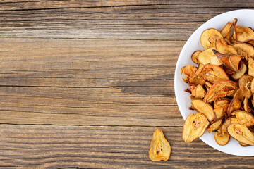 A pile of dried pears in slices on a white plate on wooden background. Dried fruit chips. Healthy food