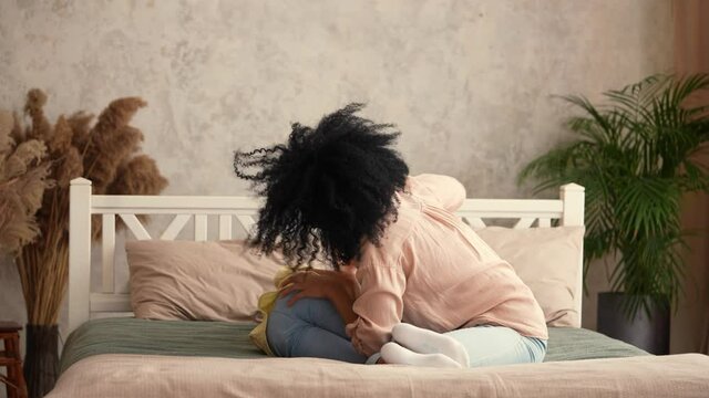 African American woman and girl have fun playing and laughing happily. Mother and daughter posing, lying on the bed in a bedroom with a bright interior. Happy family spend time together. Slow motion.
