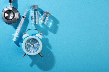 medical vaccine vials and alarm clock over blue background. time to vaccination concept.