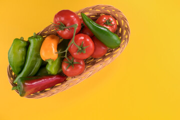 long colored peppers and tomatoes  in a wicker basket. Isolated on yellow background.Top view copy space