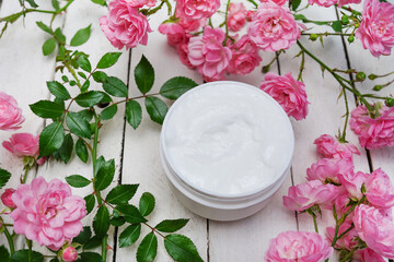 Fototapeta na wymiar cosmetic cream surrounded by pink roses on white wooden background, body skin care
