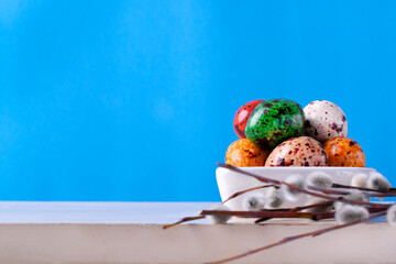 Candy Easter eggs and pussy willow twig on the white table against the blue background. Copy space