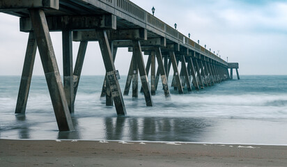 The concrete supports of an ocean pier create a pattern of intersecting lines. The long exposure of the photograph smooths out the ocean waves. Wrightsville Beach, North Carolina