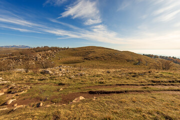 Autumn Landscape with brown meadows and small lake for cows in autumn on Lessinia High Plateau. On background the mountain range of Monte Carega. Regional Natural Park, Verona, Veneto, Italy, Europe.