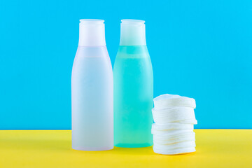 Two cosmetic bottles with micellar water and cotton pads. Facial skin care concept. Yellow and blue paper background. Makeup remover. Face toner on table, skin cleanser. Daily care, facial cleansing.