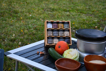Campingküche auf einem Campingtisch mit Gewürzspender, Gemüse, Kürbis, Zucchini und Kohl und...