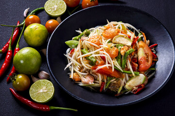 Papaya salad, Thai food cooked with papaya, tomato, green beans and peanuts Placed on a black table.