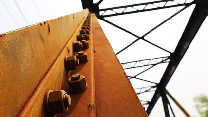 Rusted nuts and bolts on the old bridge. On the reddish-brown steel beam there are many anchor...