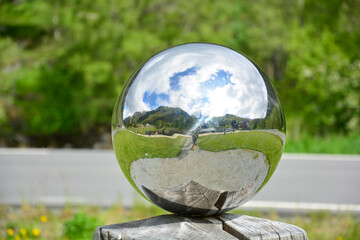 Silver ball, chromed with reflection on a wooden peg, art