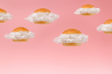 White clouds inside burger buns floating against pink sky background. Surreal fast food hamburger...
