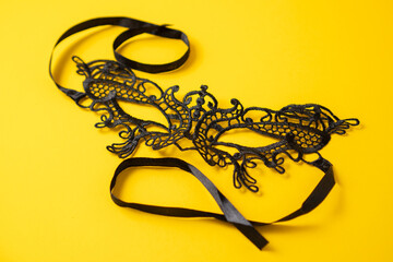 Black lace eye mask on yellow background. Delicate lace mask. Butterfly eyes mask for carnival. Close up