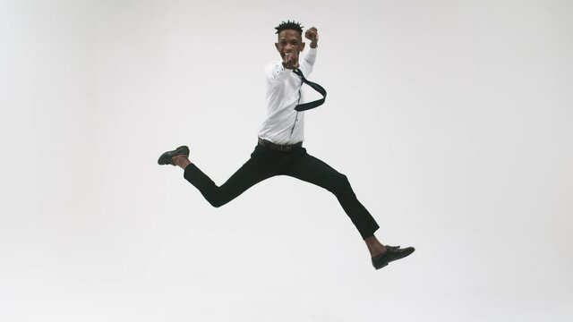 Young black man in an office suit jumps and rejoices on a white background. Black corporate office man jumping for joy in the studio.