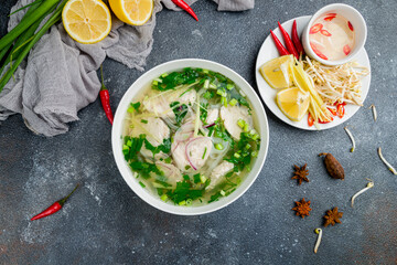 Vietnamese soup Pho GA on bowl, with chicken, green onion and spices on beautiful dark concrete...