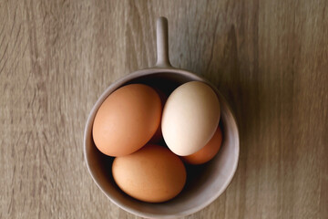 Ceramic bowl filled with fresh free range eggs on wooden table. Flat lay.