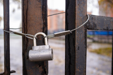 Closed padlock on an old metal rusty gate, outdoors, on a blurred background. 
