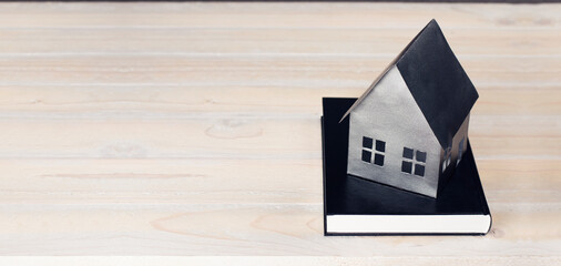 Miniature paper mock-up of a house on a book. Concept of mortgage, rent, purchase, protection, construction of a house. On a wooden background