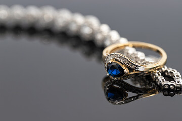 An elegant women's gold ring with blue saphire is placed on a bracelet with precious stones