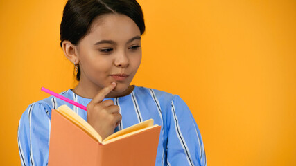 pensive kid holding pencil and notebook isolated on yellow