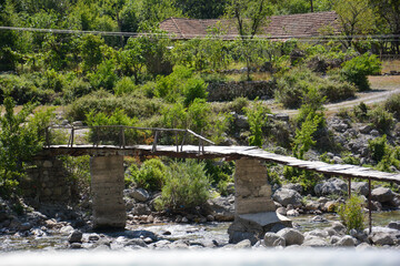Fototapeta na wymiar Alte Holzbrücke mit Steinpfosten über einen kleinen Bach im Tal bei Vermosh in Albanien