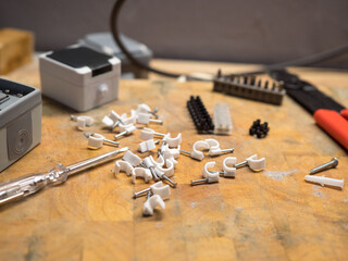 white wire clip cable clip with metal nail on wood background, workplace, workshop