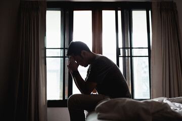 Silhouette depressed man sadly sitting on the bed in the bedroom, depression concept