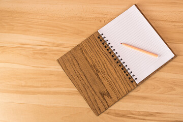 An open notepad with white pages and a brown wooden spring-bound cover lies on the table next to a cloud or pencil. View from above