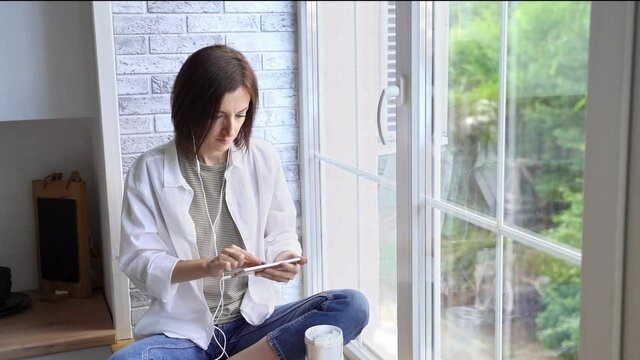 Young woman sitting at window. Working on mobile phone. Online study concept. Safety lockdown distance teaching. Female person. Quarantine office. Business writer. Video relax