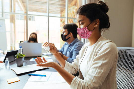 Business team wearing protective masks while meeting in the office during the COVID-19 epidemic. Woman using sanitizer gel in hand.