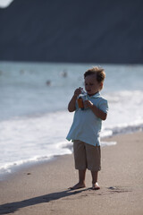 a child in beige shorts stands by the sea, holding a small glass bottle and trying to open it