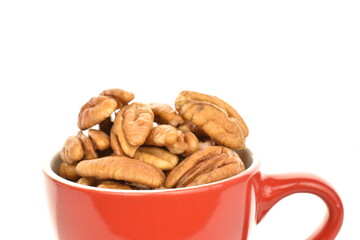 Several ripe peeled pecans in a red ceramic cup, close-up, isolated on white.