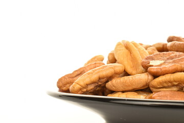 Several light brown organic shelled pecans in a black ceramic saucer, close-up, isolated on white.