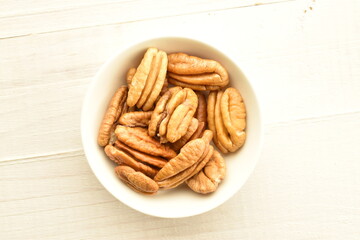 Several light brown organic peeled pecans in a white saucer on a wooden table, close-up, top view.