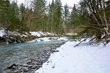 Gebirgsbach oder Fluss Breitach in Oberstdorf mit Schnee am Rand und Bäume im Hintergrund im...