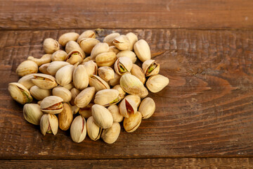 Pistachio nuts are sprinkled on a dark wooden table.
