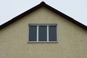 one large window on the brown concrete wall of the attic of a private house against the gray sky