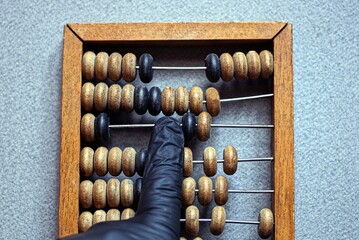 finger in black glove on brown old wooden abacus on gray table
