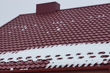 one metal chimney on a red tiled roof of a private house in white snow on a winter street against a gray sky