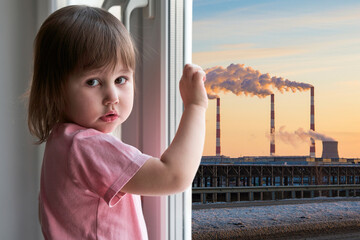 A little girl with a sad face stands at the window, outside the window is a bleak technogenic urban...