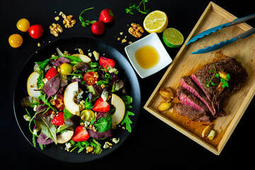 Cut steak on wooden dish with side of mixed salad with strawberries, pears, walnuts, blue cheese and lemon-honey dressing