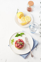 Tuna summer  tartare tartar with avocado, spices, sesame seeds, green fresh onion and lemons served on a white minimalistic dish. Summer fish menu, top view