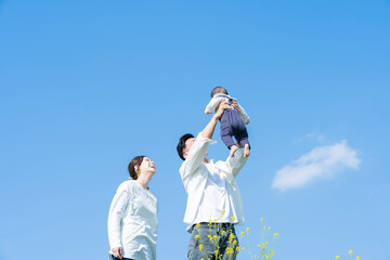 青空のもと、赤ちゃんを高く抱き上げる父母