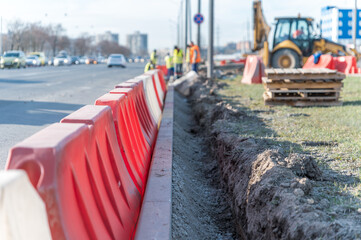 Red and white plastic safety barriers along the road and blurred workers in the background