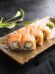 Japanese cuisine. Rolls philadelphia. Rice with red fish, avocado and cream cheese on a plate on a black table. Restaurant menu. Background image, copy space