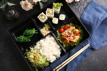 Japanese cuisine. Business lunch in a black box: rice, rolls, salad, sushi on a black table. Background image, copy space