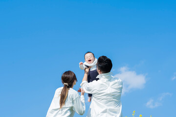 青空のもと、赤ちゃんを高く抱き上げる父母