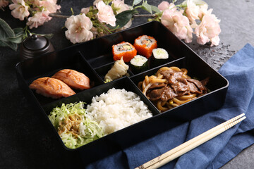 Japanese cuisine. Business lunch in a black box: rice, rolls, salad, sushi on a black table. Background image, copy space